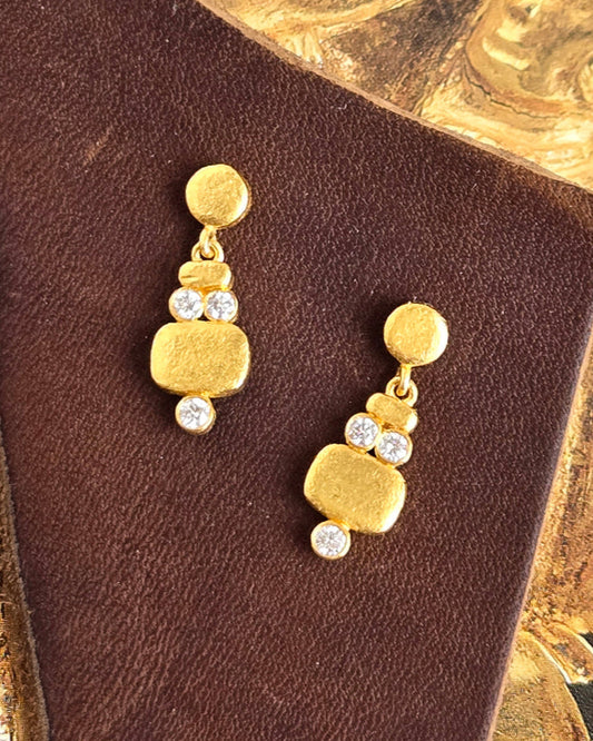 Gold earrings with clear stones on a brown card against a gold background