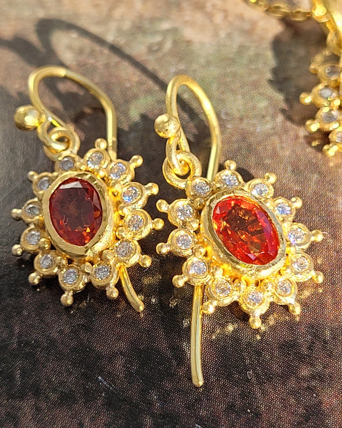 Gold earrings with red gemstones on a textured surface