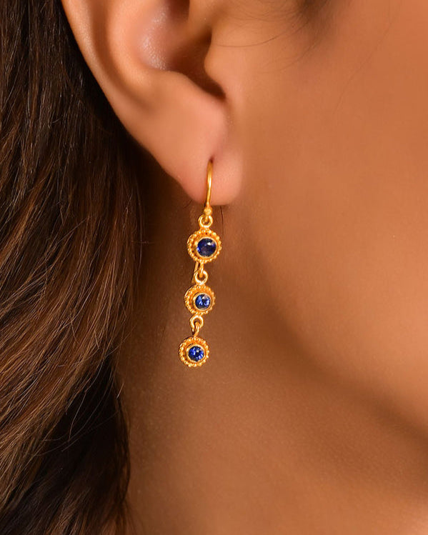 Gold earrings with blue gemstones worn by a person