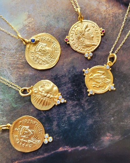 Gold coin necklaces with embedded stones on a stone surface