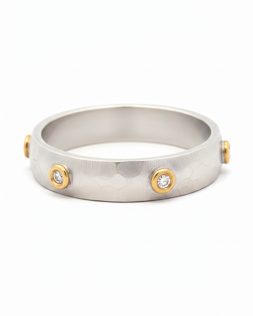 Silver ring with gold accents and embedded stones on a white background