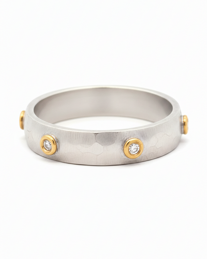 Silver ring with gold accents and embedded stones on a white background
