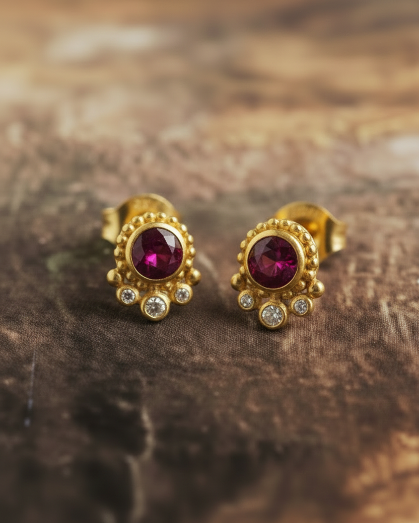 Gold earrings with red gemstones on a wooden surface